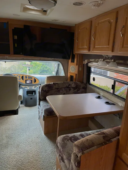 Interior view of an RV rental, featuring a comfortable dinette, front driving area, TV, and wooden storage.. Concord Coachmen 2004
