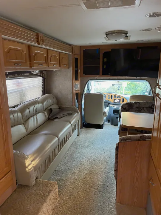Inviting RV rental interior featuring a beige sofa, dining area, and driver's cockpit. Explore in comfort!. Concord Coachmen 2004