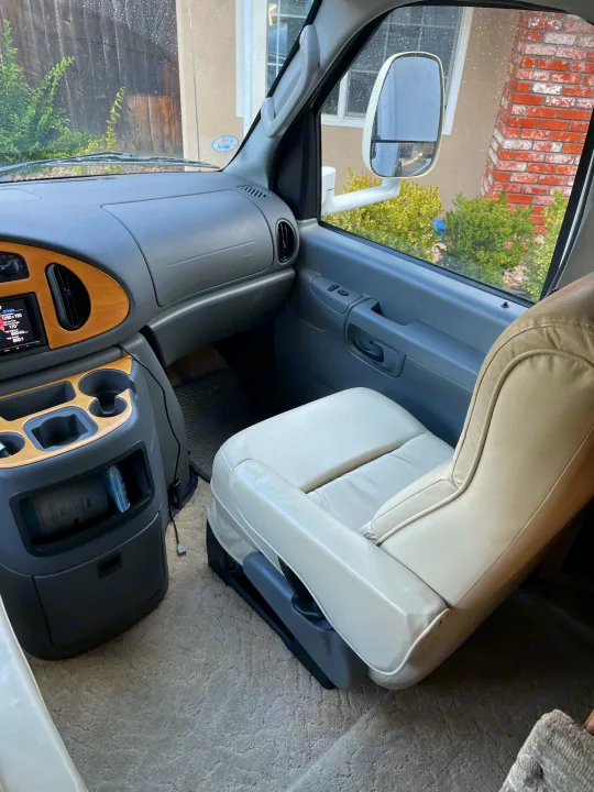 Interior of an RV rental, highlighting the front passenger seat, dashboard, and console with cup holders, seen through wet windows.. Concord Coachmen 2004