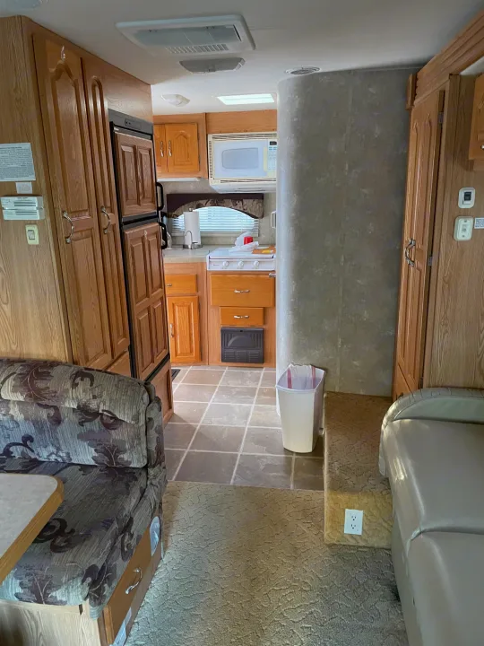 View inside an RV rental showing a full kitchen with microwave, fridge, stove, and living area with patterned and plain sofas.. Concord Coachmen 2004