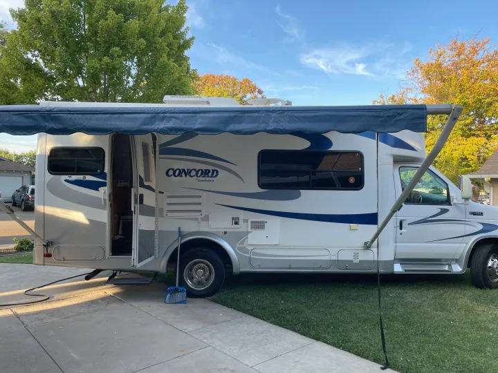 A white and blue Concord Coachmen RV rental, parked with its awning extended and door open, ready for your next trip.. Concord Coachmen 2004