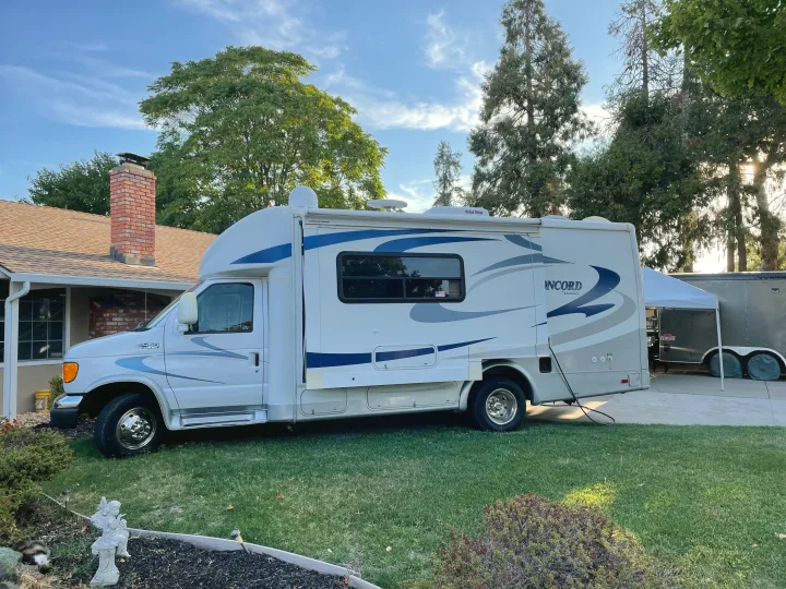 A white and blue RV parked on a lawn by a house & trailer. Consider this rv rental for your next adventure!. Concord Coachmen 2004