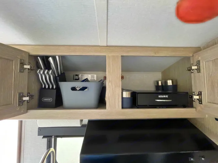 Organized RV rental kitchen cabinet with knife block, storage bin, and Keurig coffee maker above the range hood.. Forest River GeoPro 2021
