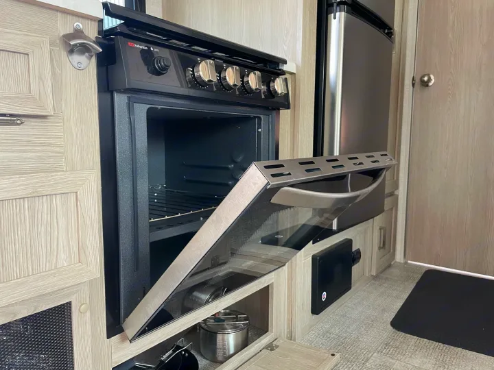 RV rental kitchen details: open oven, compact fridge, and convenient wall-mounted bottle opener on light wood cabinets.. Forest River GeoPro 2021