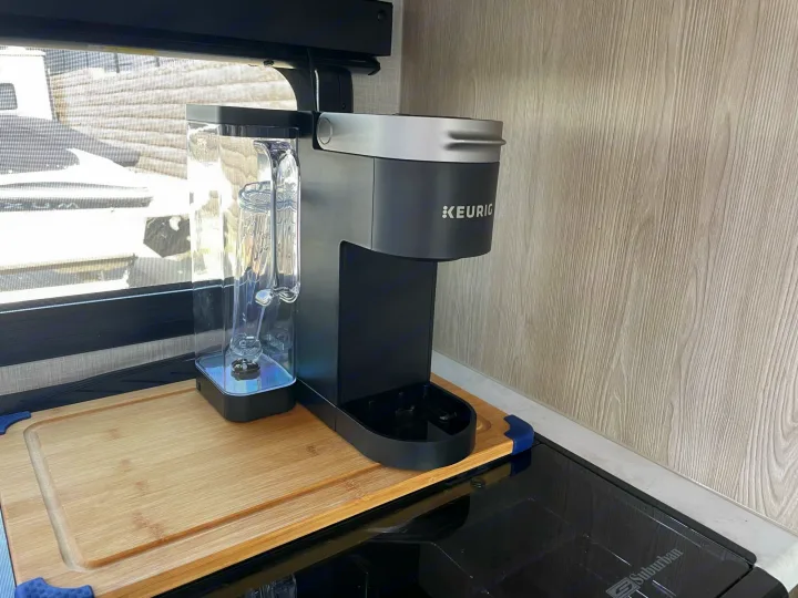 Keurig coffee maker on wood cutting board in RV rental kitchen, with window & cooktop nearby.. Forest River GeoPro 2021