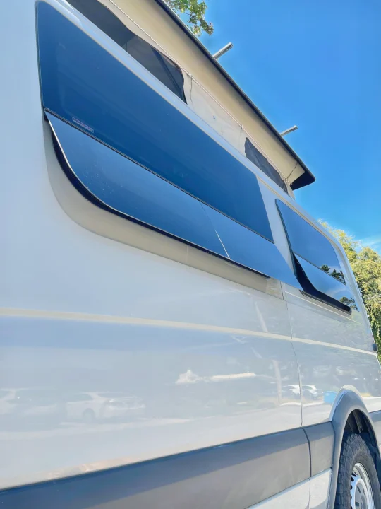 Side view of a modern white camper van with large dark windows and a raised pop-top roof, perfect for an RV rental adventure.. Sportsmobile Custom Design 2013