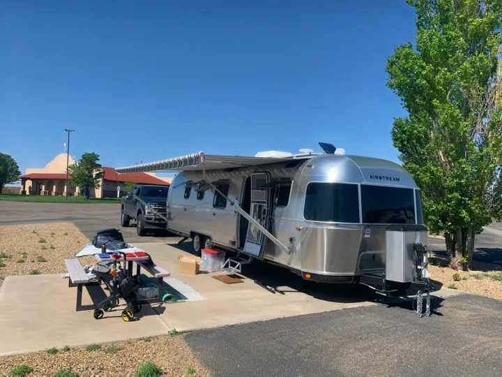 A silver Airstream RV at a sunny RV park. This RV rental is set up with an awning, picnic table, and truck.. Airstream Classic 2021