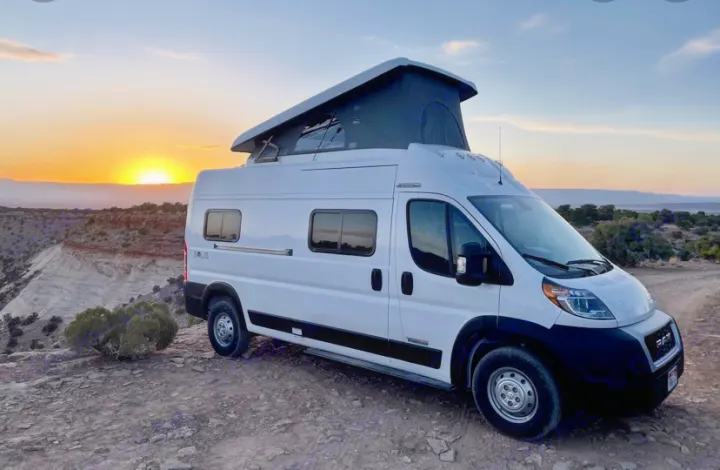 Witness a stunning sunset from this Winnebago Solis pop-top camper van, ideal for your next RV rental adventure on rugged terrain.. Winnebago Solis 2021