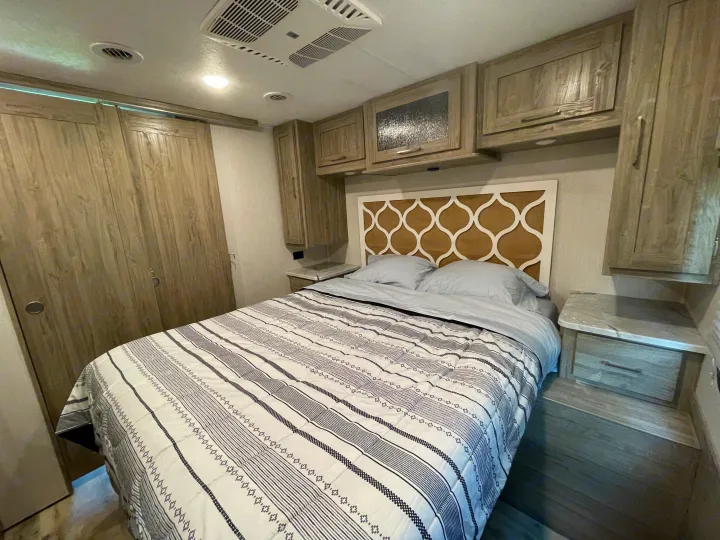 Cozy RV rental bedroom with patterned comforter, overhead storage, and wardrobe.. Coachmen Pursuit 2021