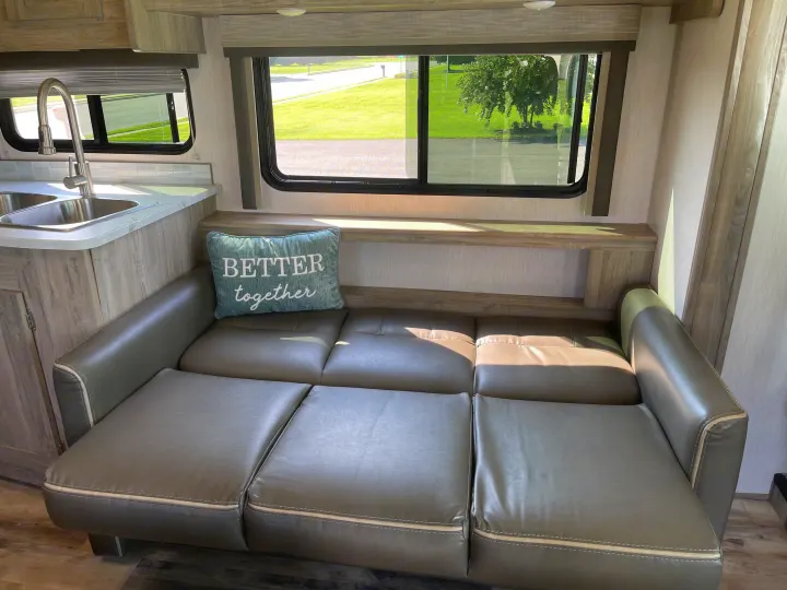 RV rental interior: comfy convertible sofa, functional kitchen sink, and bright window view.. Coachmen Pursuit 2021