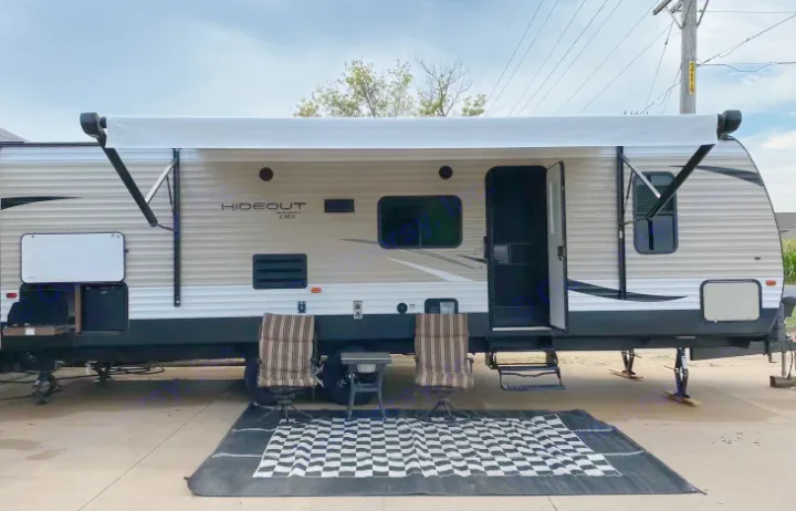 This light-colored rv rental, a travel trailer, features an extended awning, outdoor kitchen, and comfortable seating at a campsite.. Keystone Hideout 2019