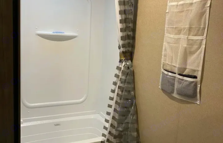 Compact RV rental bathroom: white shower/tub, tied patterned curtain, and wall-mounted mesh organizer for storage.. Keystone Hideout 2019