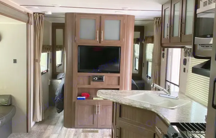 Inside a spacious RV rental, showcasing a functional kitchen, entertainment center, and private bedroom area.. Keystone Hideout 2019