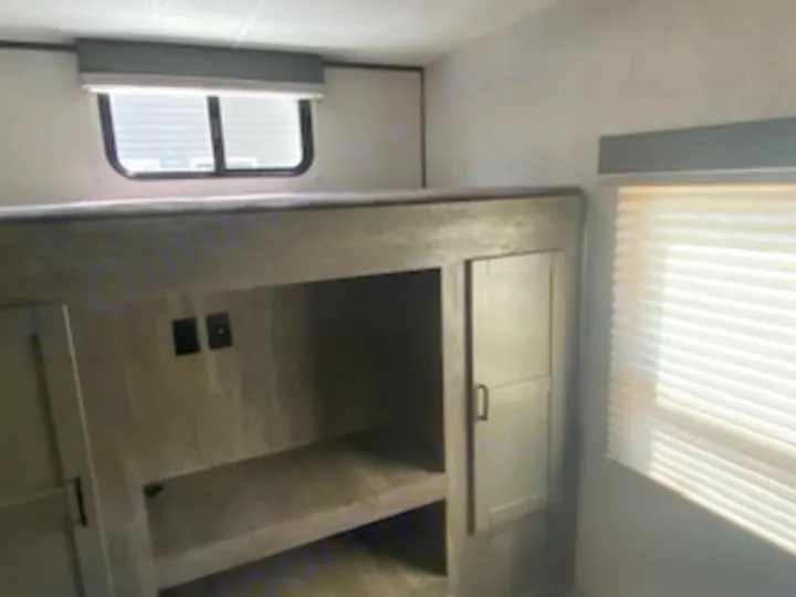 RV rental bunk room with a top bed, lower storage/entertainment area, and cabinets, well-lit by windows.. Heartland RVs North Trail 2020