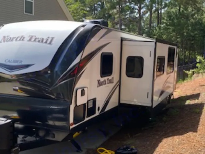 Modern white North Trail travel trailer RV rental, parked outdoors with its side slide-out extended for more space.. Heartland RVs North Trail 2020