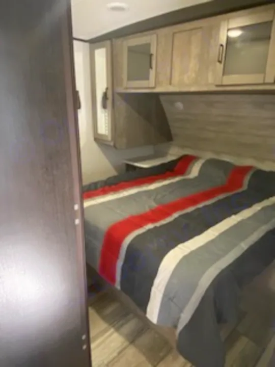 This RV rental bedroom features a bed with a vibrant striped comforter, surrounded by modern storage cabinets and wood-look flooring.. Heartland RVs North Trail 2020