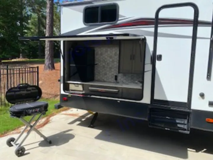 This RV rental's side compartment reveals an outdoor kitchen with a sink, fridge, and storage, alongside a portable grill.. Heartland RVs North Trail 2020