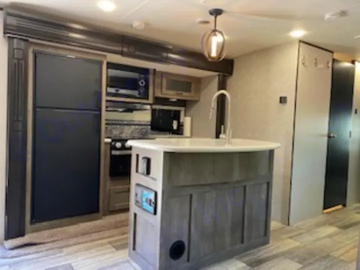 Step inside this RV rental's modern kitchen area, featuring a large fridge, stove, and island with sink, offering a spacious interior.. Heartland RVs North Trail 2020