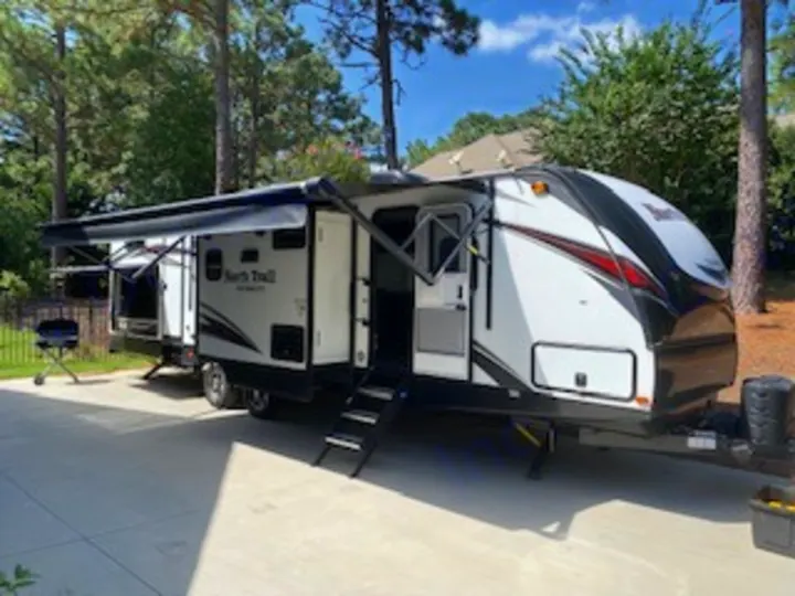 This RV rental, a sleek travel trailer with awnings extended, is ready for your outdoor adventures. Perfect for camping trips!. Heartland RVs North Trail 2020
