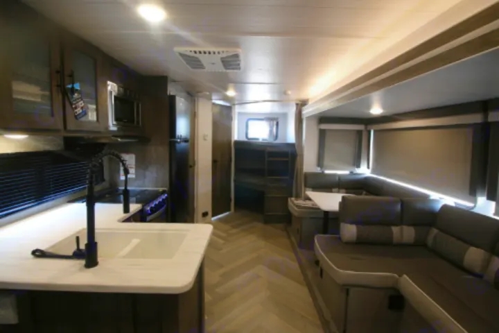 Inside a modern RV rental: a well-equipped kitchen, spacious living area with U-shaped sofa, and bunk beds visible for travelers.. Forest River Salem 2023