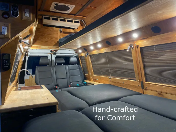 Cozy RV rental interior with custom wood trim, a functional kitchen, and comfortable bed. Hand-crafted for comfort.. Ford Econoline 2011