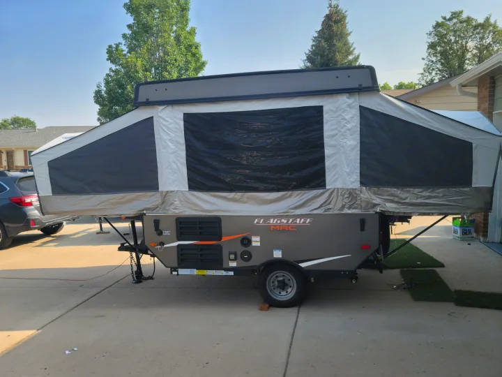 A grey Flagstaff pop-up camper, similar to an RV rental, is fully set up in a driveway under a clear sky, ready for camping.. Forest River Flagstaff 2021