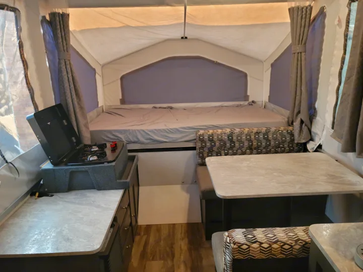 Inside an RV rental: cozy bed area, compact kitchen stove, and a dinette with patterned cushions.. Forest River Flagstaff 2021