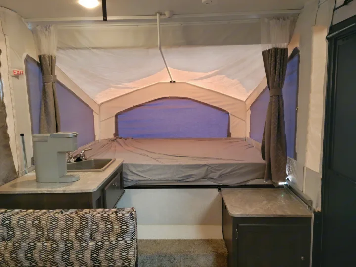 Spacious pop-up camper interior for RV rental: comfortable bed, kitchen sink with coffee maker, and patterned dinette.. Forest River Flagstaff 2021