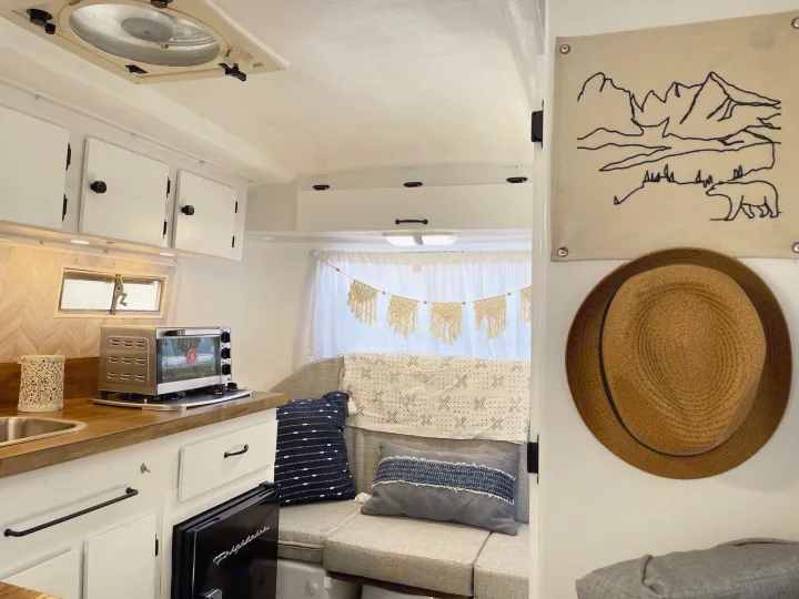 Bright RV rental interior, showing a compact kitchen, comfy bench seating, and charming wall decor.. Scamp 13' 1979