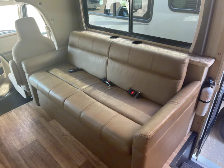 RV rental interior showcasing a light-colored couch with seatbelts, window, built-in cup holders, and a fire extinguisher.. Thor Four Winds 2021
