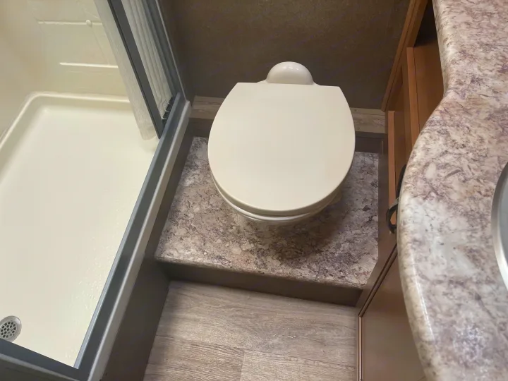 Spacious RV rental bathroom featuring a white toilet, a shower, and a practical speckled countertop vanity.. Thor Four Winds 2021