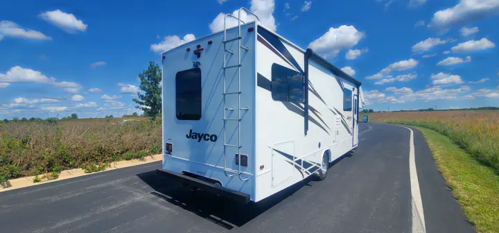 White Jayco motorhome RV rental parked on asphalt, under a blue sky with clouds. Perfect for road trips!. Jayco Redhawk 2021