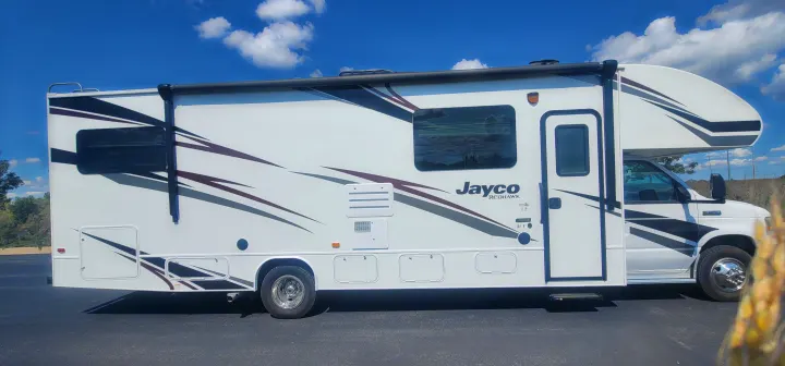 Side view of a white Class C Jayco Redhawk motorhome with grey, black, and maroon graphics, ideal for rv rental adventures.. Jayco Redhawk 2021