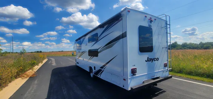This white Jayco RV rental motorhome awaits your next road trip adventure, parked outdoors under a blue sky and clouds.. Jayco Redhawk 2021