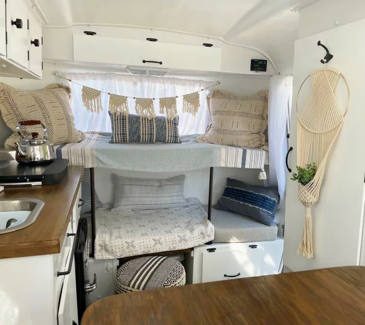 Stylish RV rental interior: bunk beds with boho decor, compact kitchen with sink and stovetop, and clean design.. Scamp 13' 1979