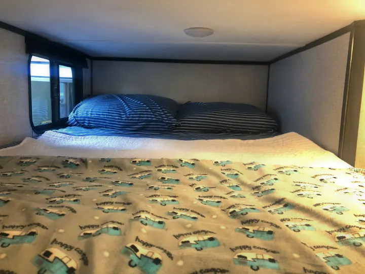 Comfortable sleeping area in an RV rental, featuring blue striped pillows and a "happy camper" blanket.. Dutchman Aspen Trail 2022