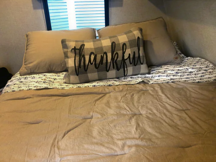 Cozy RV rental bed with "Thankful" pillow and camper-themed sheets.. Dutchman Aspen Trail 2022
