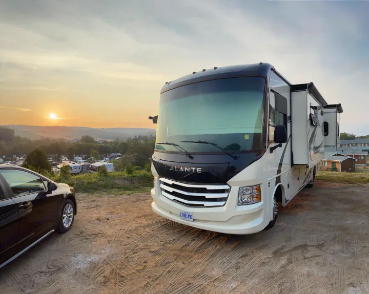 Experience an RV rental adventure! A large Alante motorhome and car are parked at a scenic campground, bathed in the soft light of sunset.. Jayco Other 2021