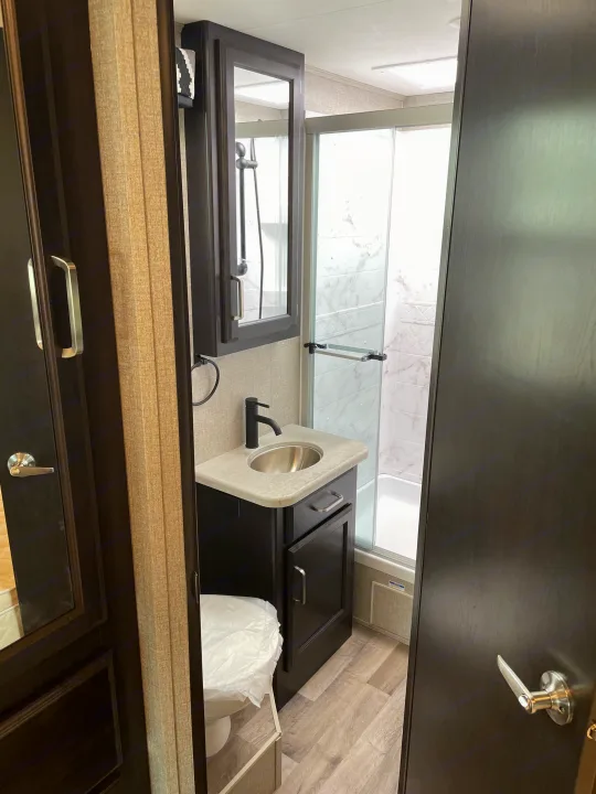 Modern RV rental bathroom: dark vanity, stainless sink, glass shower, and covered toilet.. Jayco Other 2021