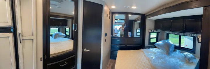 Inside an RV rental's bedroom: a clean bed with new pillows, mirrored wardrobe, and dark wood cabinets for comfortable travel.. Jayco Other 2021