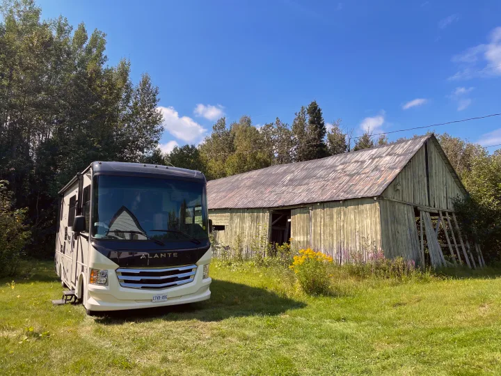An RV rental is parked on a grassy field next to an old barn, surrounded by lush trees under a clear blue sky. Ideal for nature lovers.. Jayco Other 2021