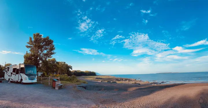 RV rental parked by a fence, overlooking a rocky beach & calm blue water under a bright sky with clouds.. Jayco Other 2021