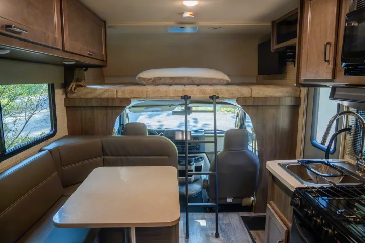 Explore the cozy interior of this rv rental, featuring an overhead bunk bed, dinette with seating, and a compact kitchen.. Winnebago Minnie Winnie 2021