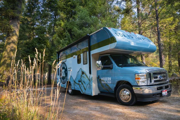 Light blue Modern Road Trip RV rental on a sunlit forest path. Perfect for your next nature adventure.. Winnebago Minnie Winnie 2021