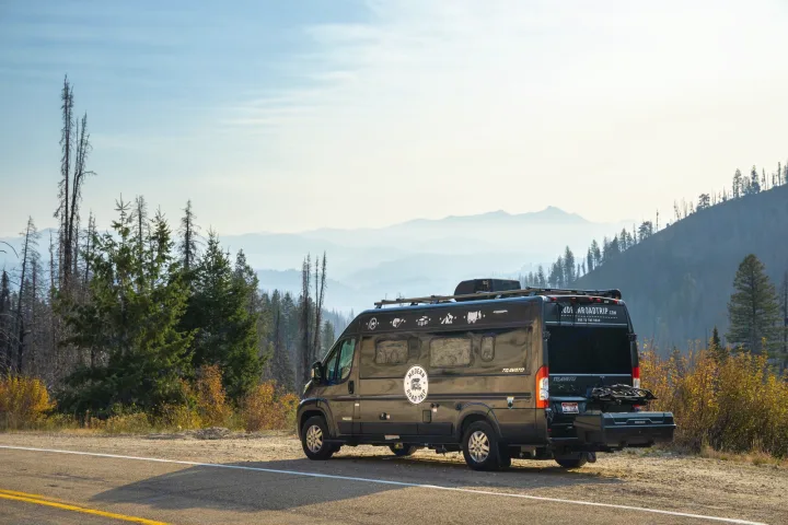 Black RV rental parked roadside on a mountain road, with majestic hazy peaks and fall foliage.. Winnebago Other 2021