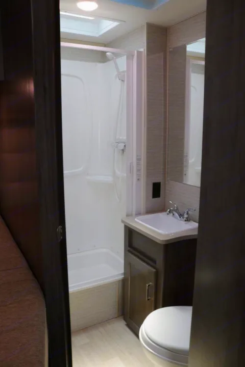 Compact RV rental bathroom featuring a corner shower, sink vanity, and toilet.. Winnebago Minnie Winnie 2021