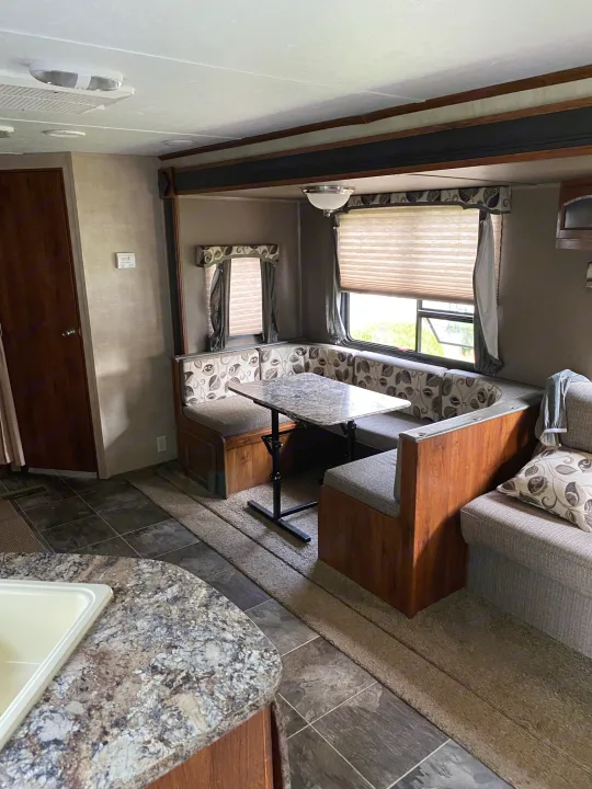 Spacious RV rental interior featuring a dinette booth, sofa, and kitchen counter, ideal for comfortable travel.. Keystone Hideout 2014