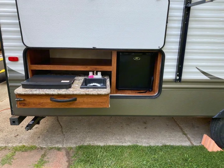 Outdoor kitchen setup on an RV rental with a pull-out counter, cooking surface, sink, and mini-fridge.. Keystone Hideout 2014