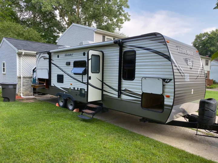 A large Hideout by Keystone travel trailer RV rental is parked on a residential driveway, ready for its next adventure.. Keystone Hideout 2014