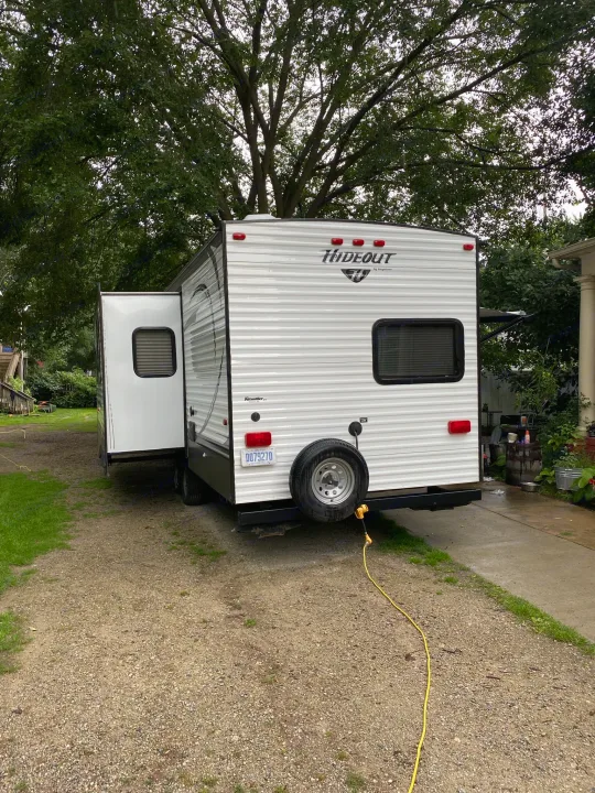 A white Hideout travel trailer, potentially an RV rental, is parked on a gravel driveway with its side slide-out extended.. Keystone Hideout 2014